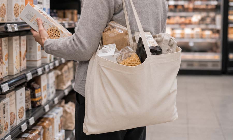 Oblekt tygkasse med förpackningar i matbutik Oblekt tygkasse med långa handtag fylld med förpackningar i matbutik